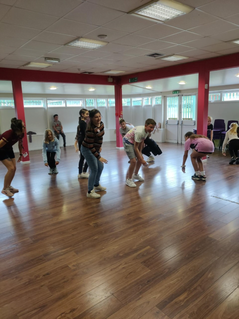 Students participating in a dance or movement class at King Edward VI Balaam Wood Academy. Children are adjusting into position in a spacious studio with wooden flooring and bright lighting.