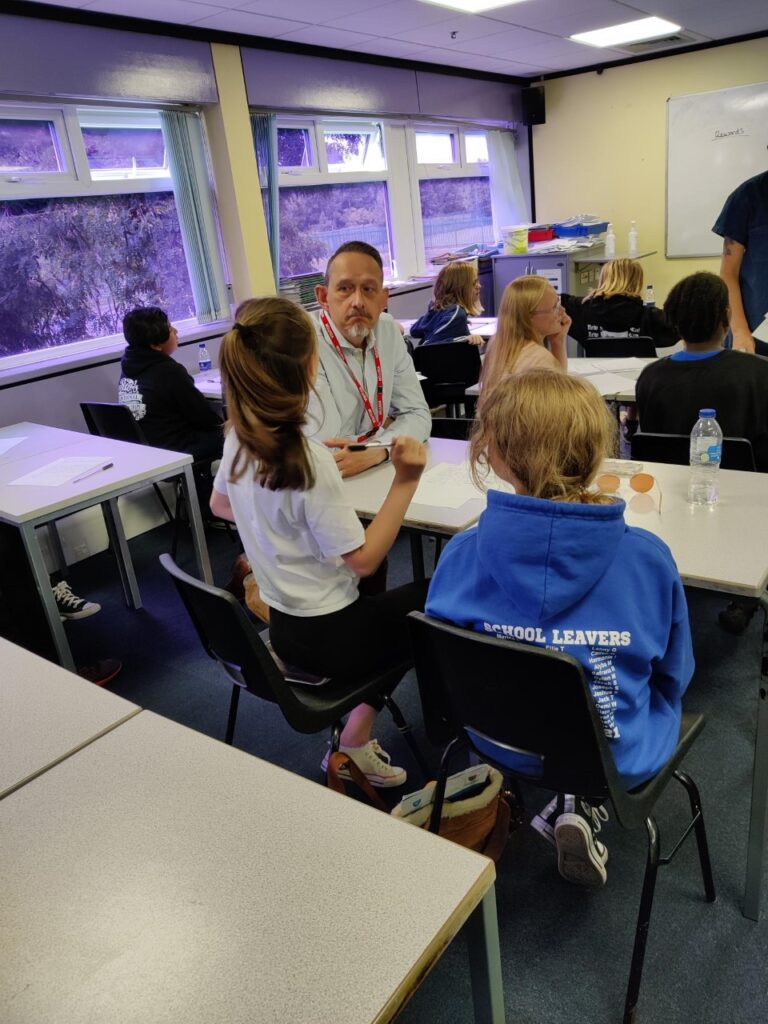 Students interacting with a teacher in a classroom at King Edward VI Balaam Wood Academy, showcasing educational engagement and campus life.